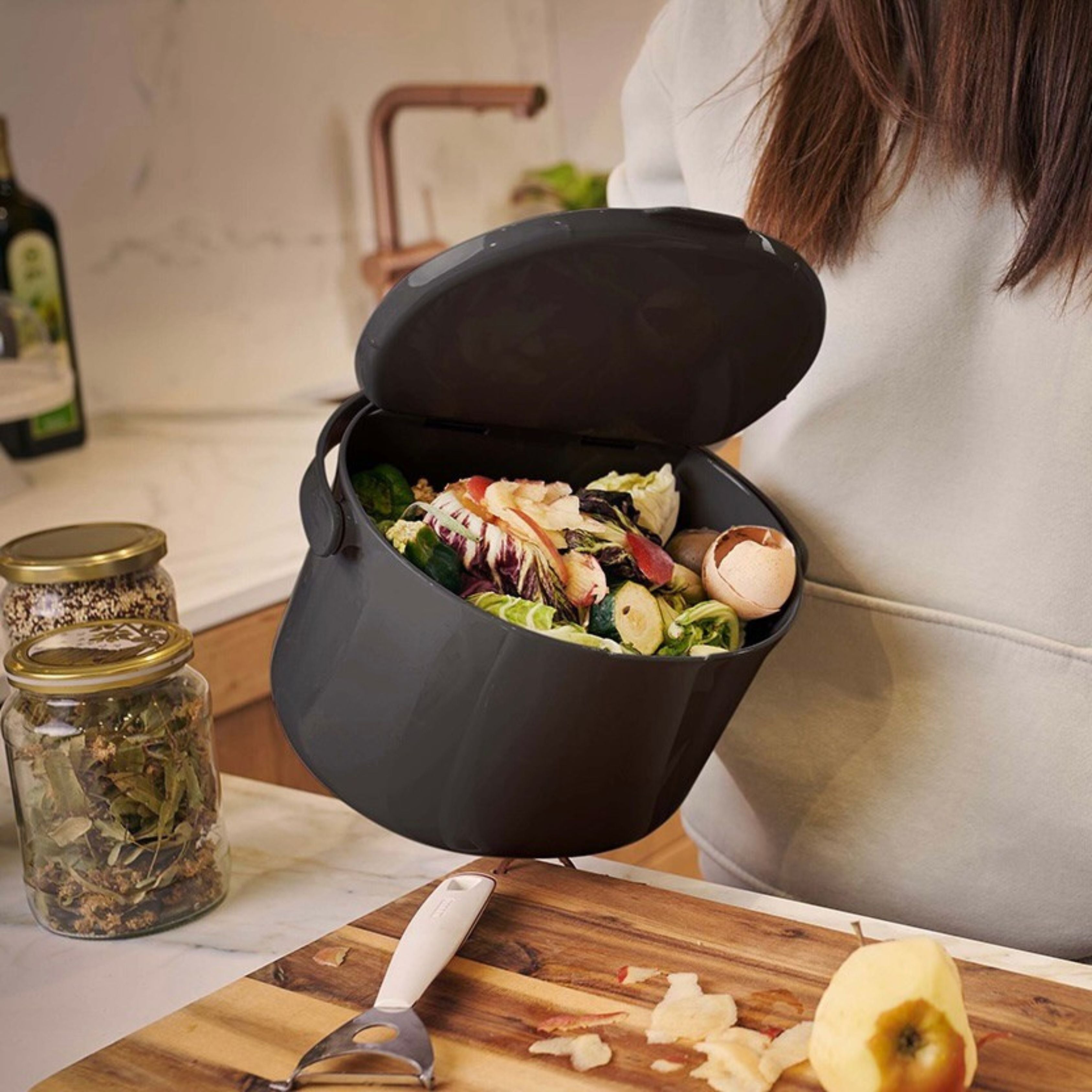 A woman holds an Organko Daily trash bin full of biowaste, which looks very comfortable to hold thanks to its ergonomic, securely attached handle